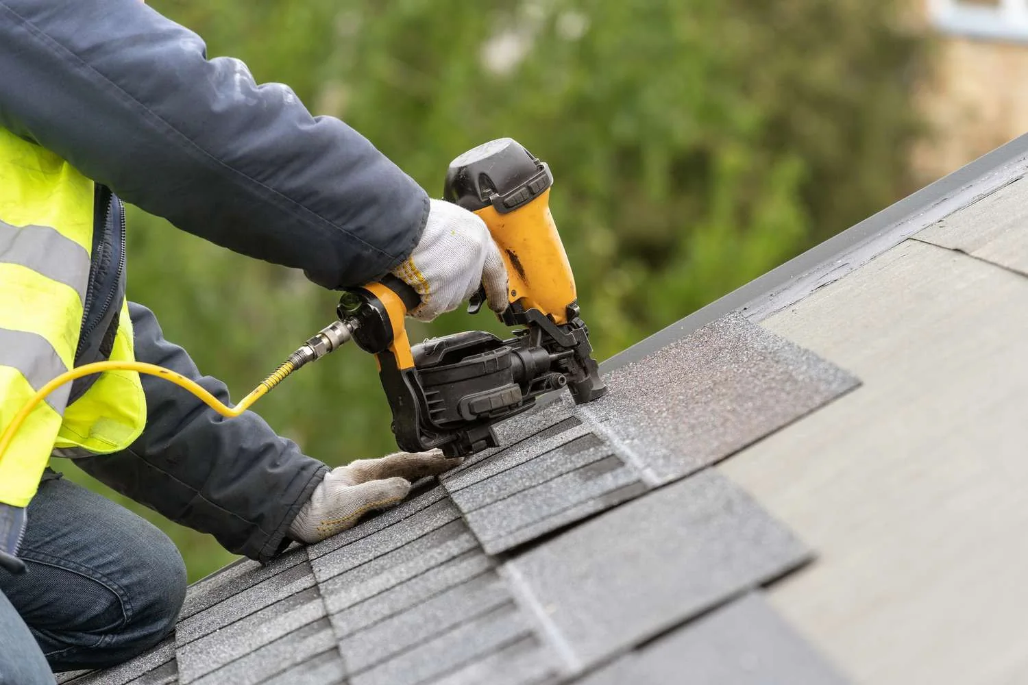 Roofing contractor in a hi-vis vest using a nail gun to fasten asphalt shingles on a San Antonio roof