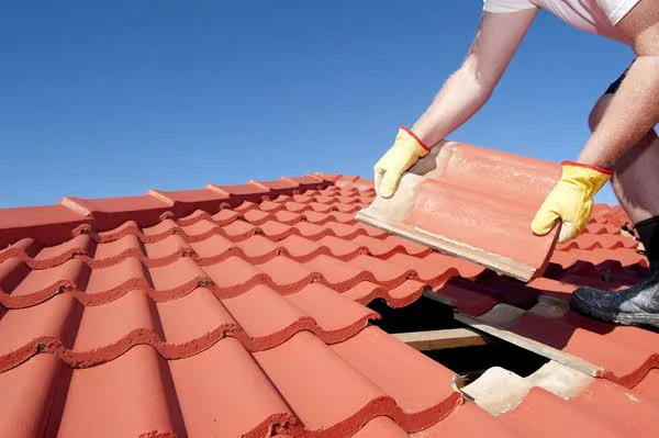 Roofer lifting a clay roof tile to reach the damaged battens and underlayment beneath